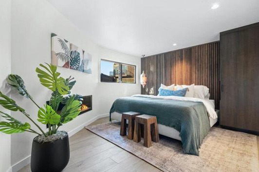 A geodome bedroom after renovation: green bedding, a dark slatted timber wall and a linear fireplace.
