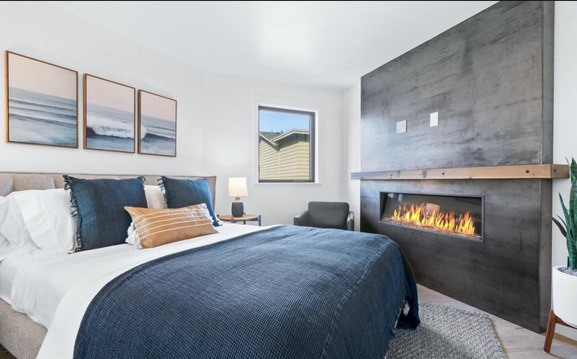 A geodome bedroom after renovation: navy bedding and a linear fireplace set into a board-formed concrete wall.