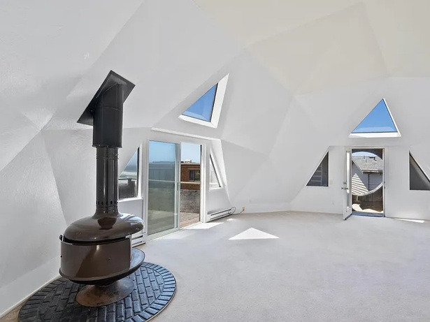 Another empty dome room before renovation, with a wood-burning stove and triangular windows.