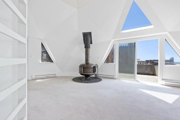 The main dome before renovation: an empty carpeted room with a wood stove and built-in shelving.