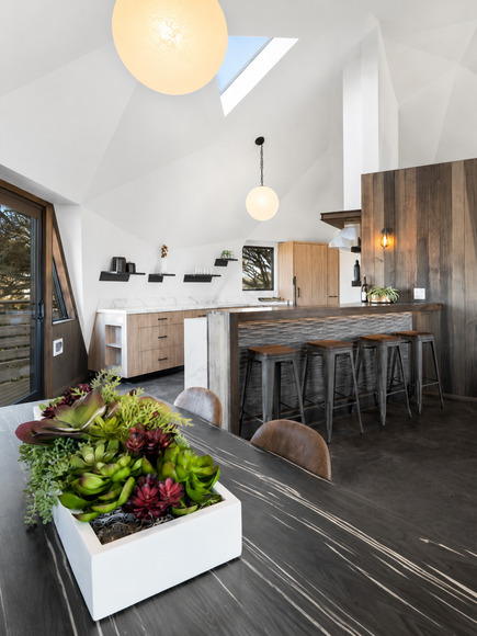 The geodome kitchen and dining area after renovation, with a timber island, metal stools and pendant lights under the vaulted white ceiling.