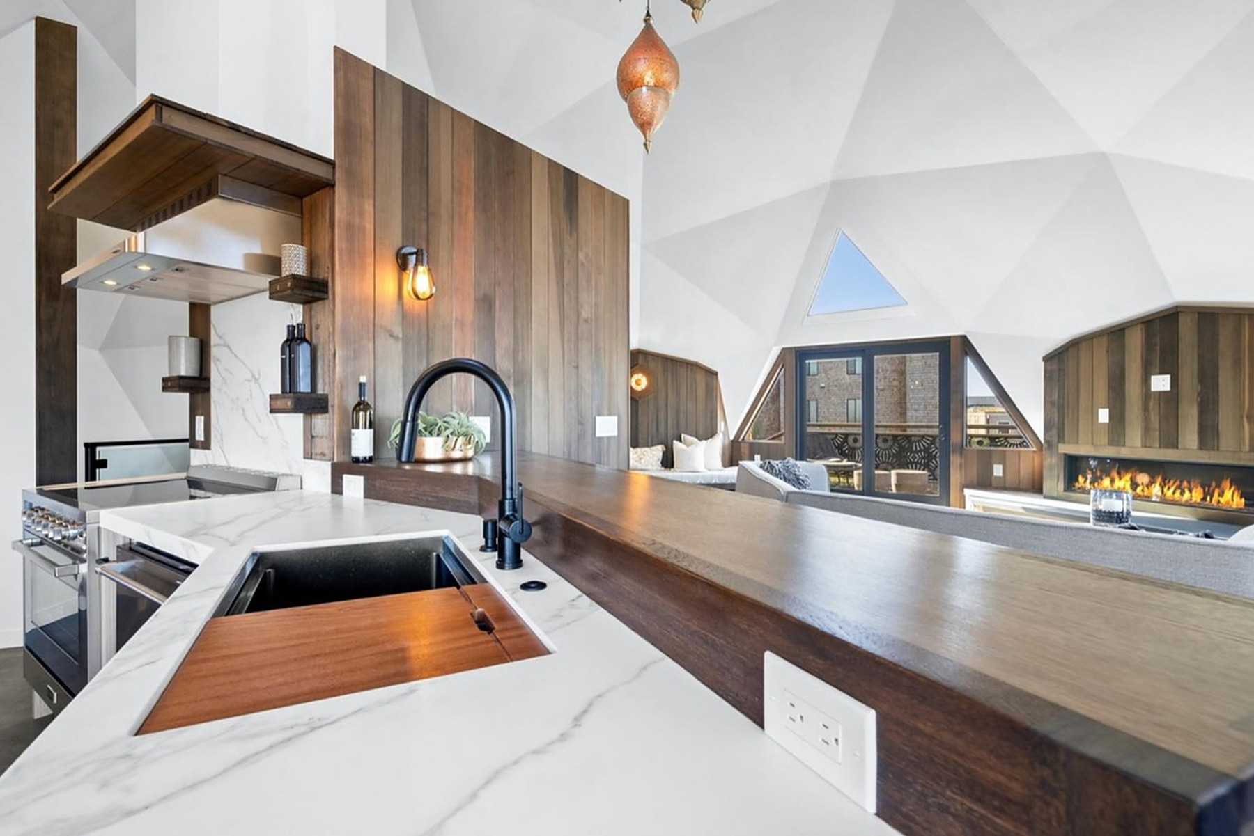 The finished Pajaro Dunes geodome kitchen: a marble waterfall counter and walnut cladding under the faceted white dome ceiling.
