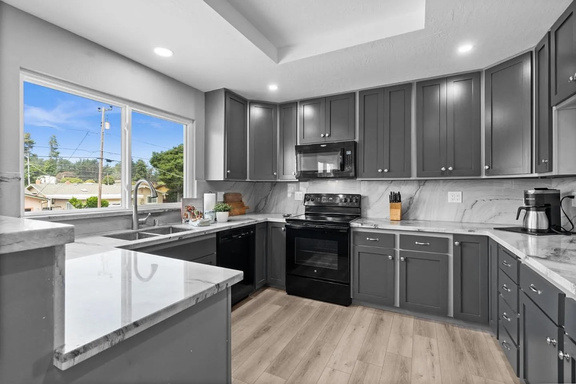 The original kitchen before renovation: grey cabinets, black appliances and a peninsula under a window.