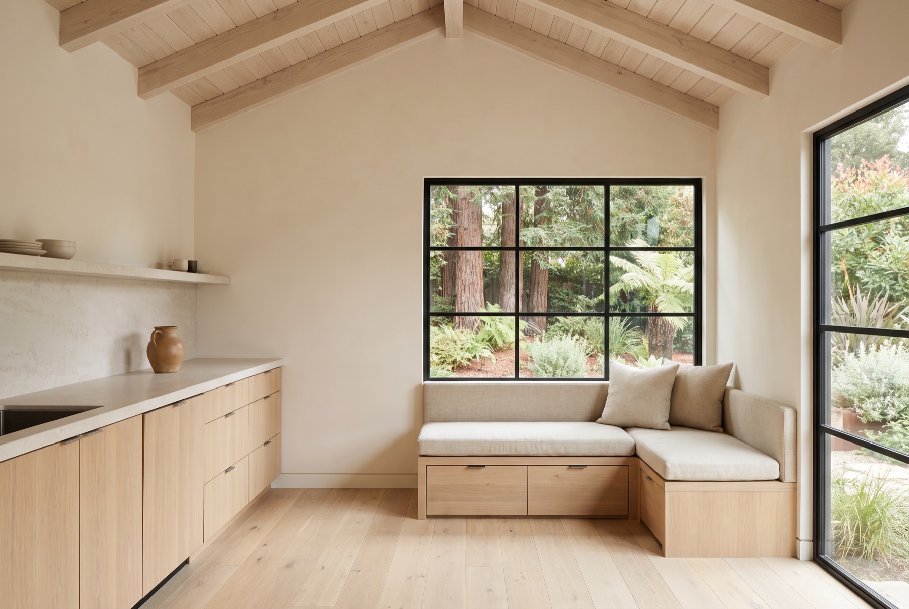 A compact ADU interior with a white oak kitchenette, built-in bench seating and a vaulted timber ceiling.