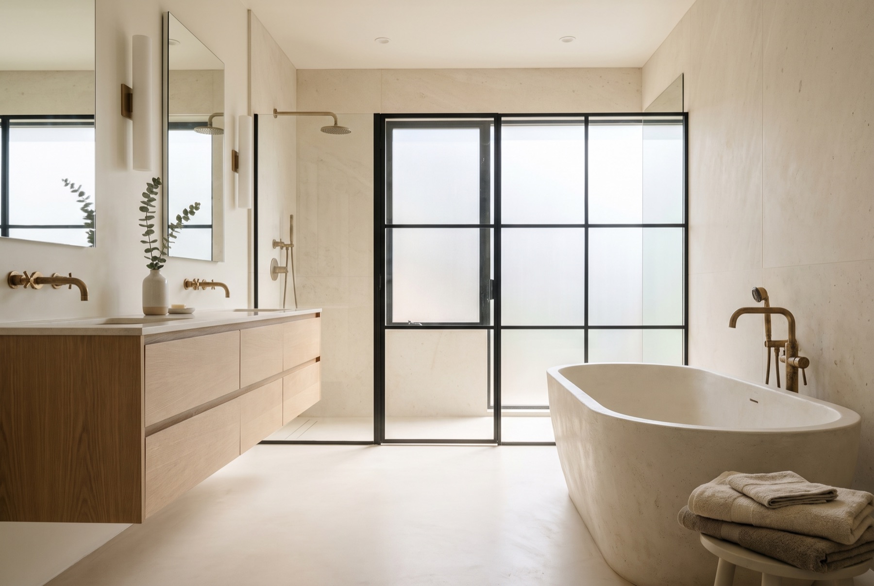 A limestone wet room with a floating white oak double vanity, brass tapware and a freestanding tub.