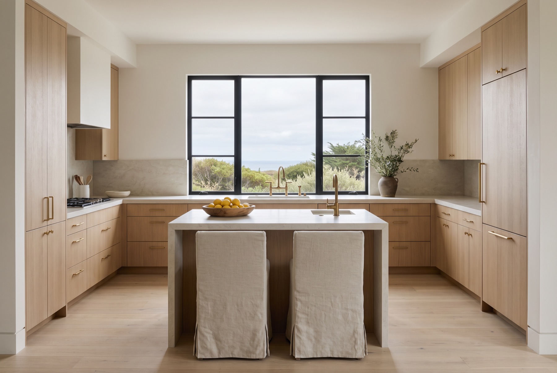 A white oak kitchen with a honed limestone island, brass fixtures and a black steel window over the sink.